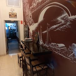 Mesa alta e bancos junto à parede bordô com ilustração de ponte e barcos