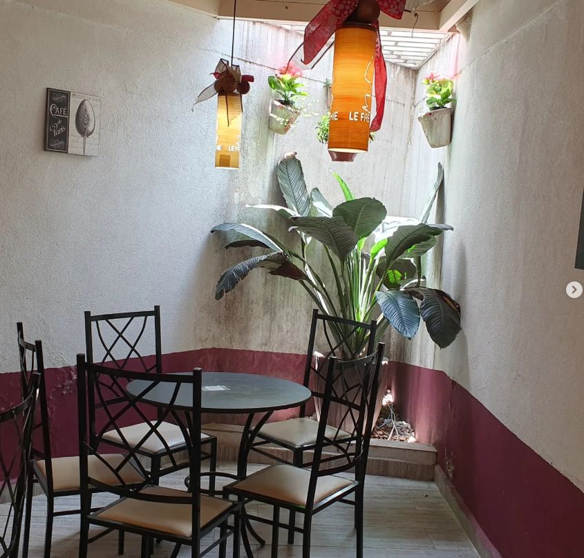 Canto do salão com mesa de ferro, cadeiras e plantas sob luz natural